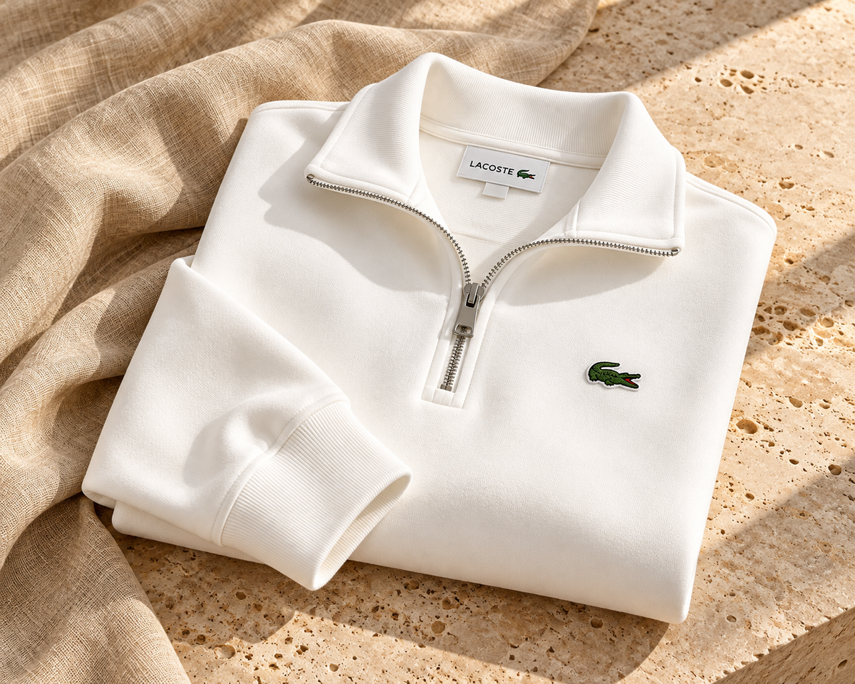 Buzo blanco Lacoste Quarter Zip doblado sobre piedra travertino